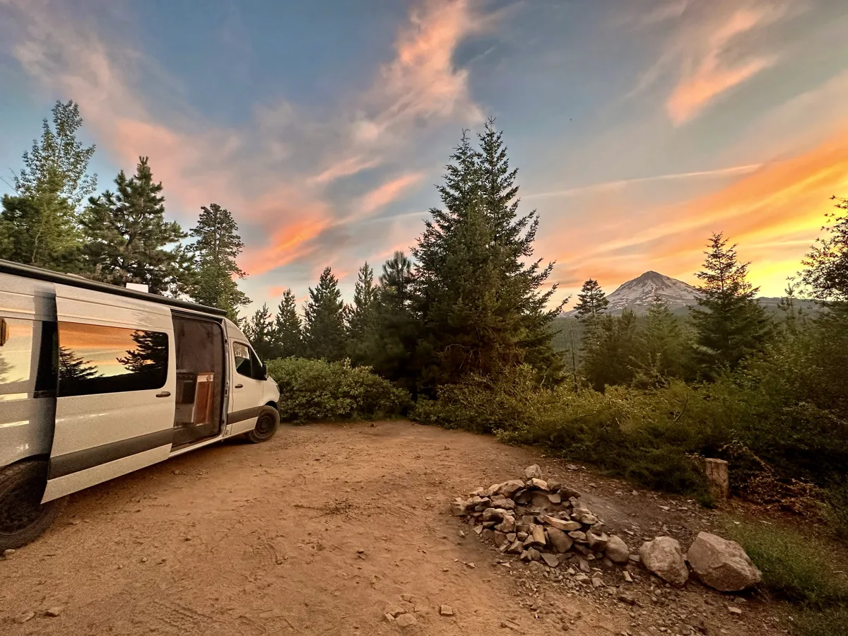 Pebbles at a forest campsite with mountains and sunset beyond