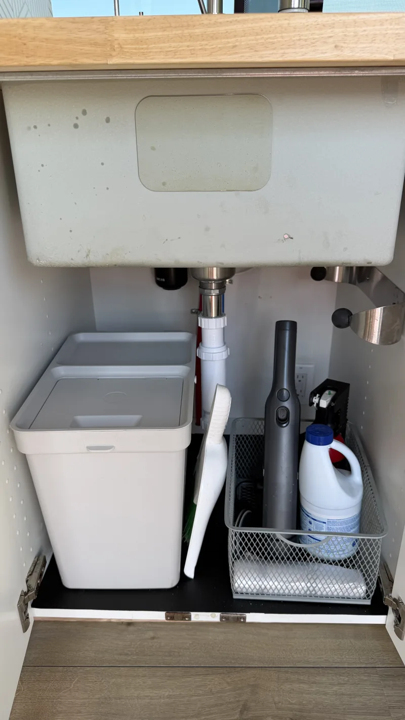 Under-sink cabinet open to show plumbing and storage