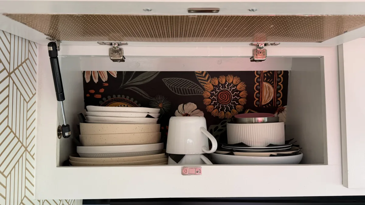 Left upper kitchen cabinet open with dishes and mugs