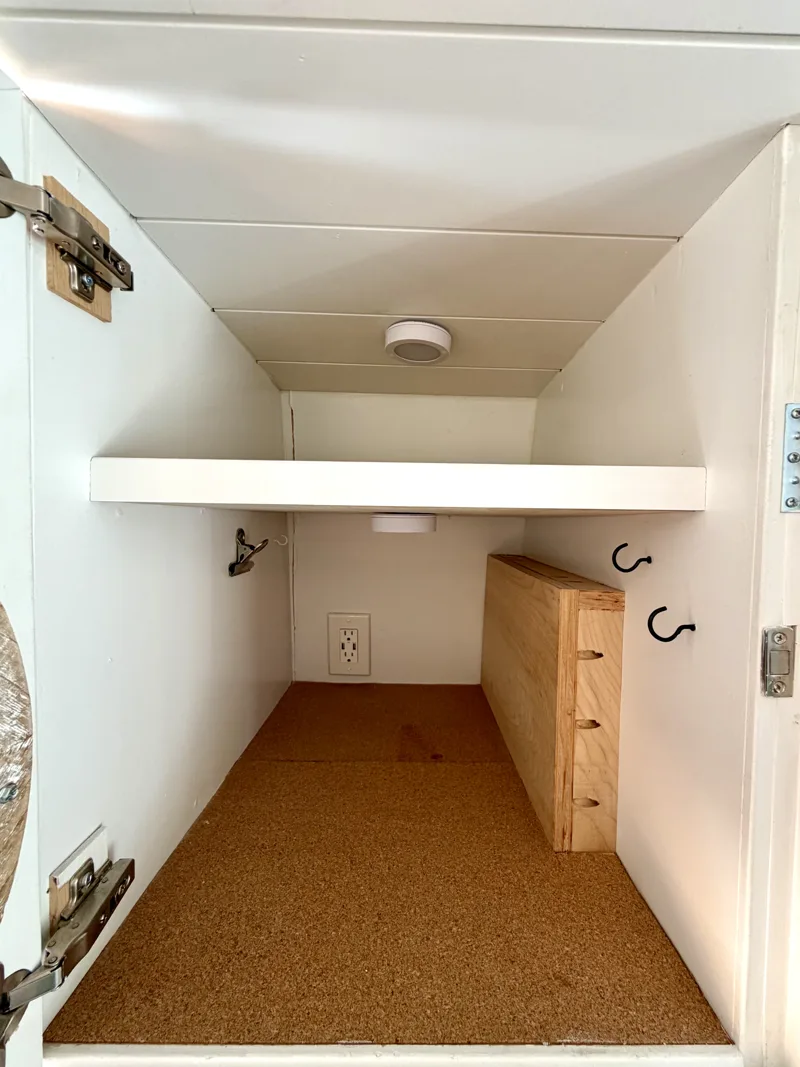 Inside the vanity cabinet showing shelves, hooks, and an outlet